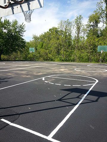 A basketball court with a basketball hoop and trees in the background