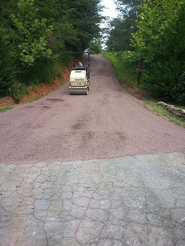 A roller is rolling gravel down a dirt road.