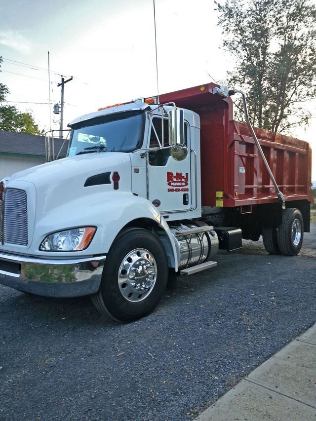 A white dump truck with a red bed is parked on the side of the road.