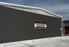 Gray self-storage building with a red-and-white sign under a cloudy sky