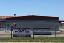 AAA Storage building with sign in front, gray and red exterior behind chain-link fence.