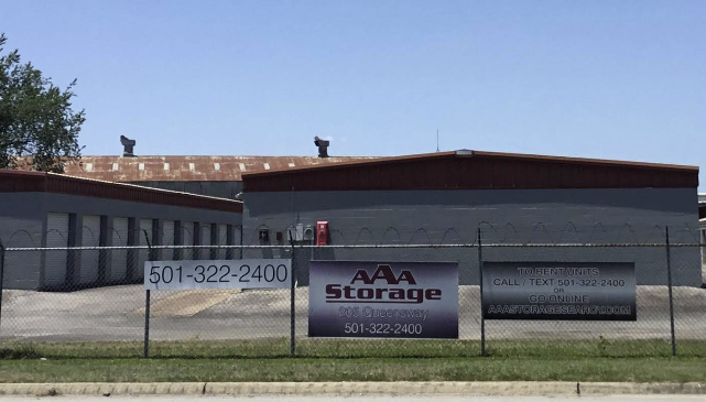 AAA Storage building with gray walls and red roof behind a roadside sign under a clear sky