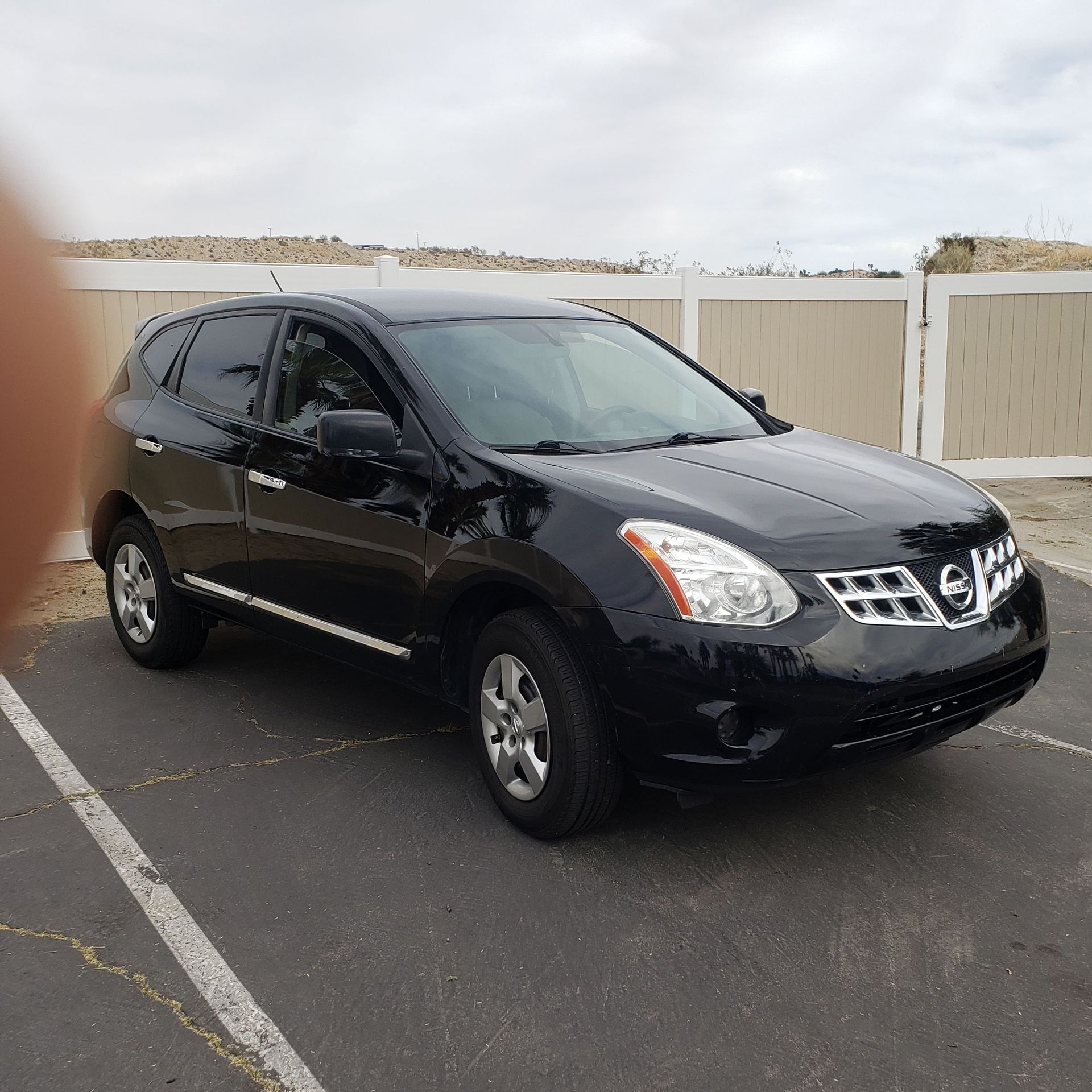 Black SUV parked in a lot beside a white fence under an overcast sky