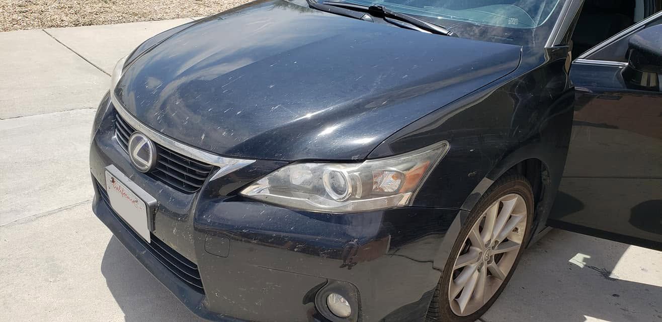 Black Lexus sedan parked on a sunny driveway, front-left view with minor bumper damage