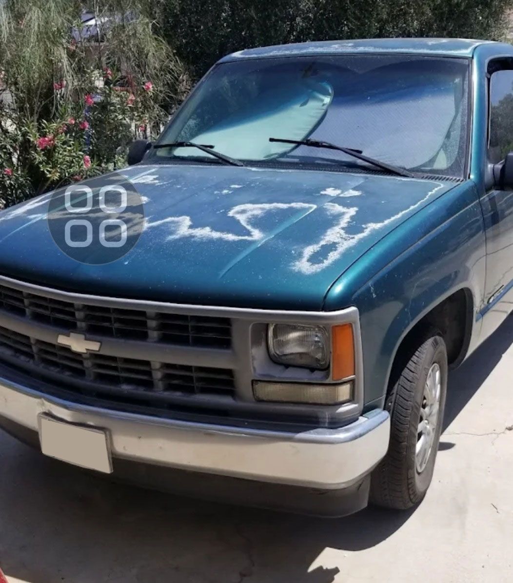 Blue pickup truck parked outdoors in bright sunlight with white markings on the hood