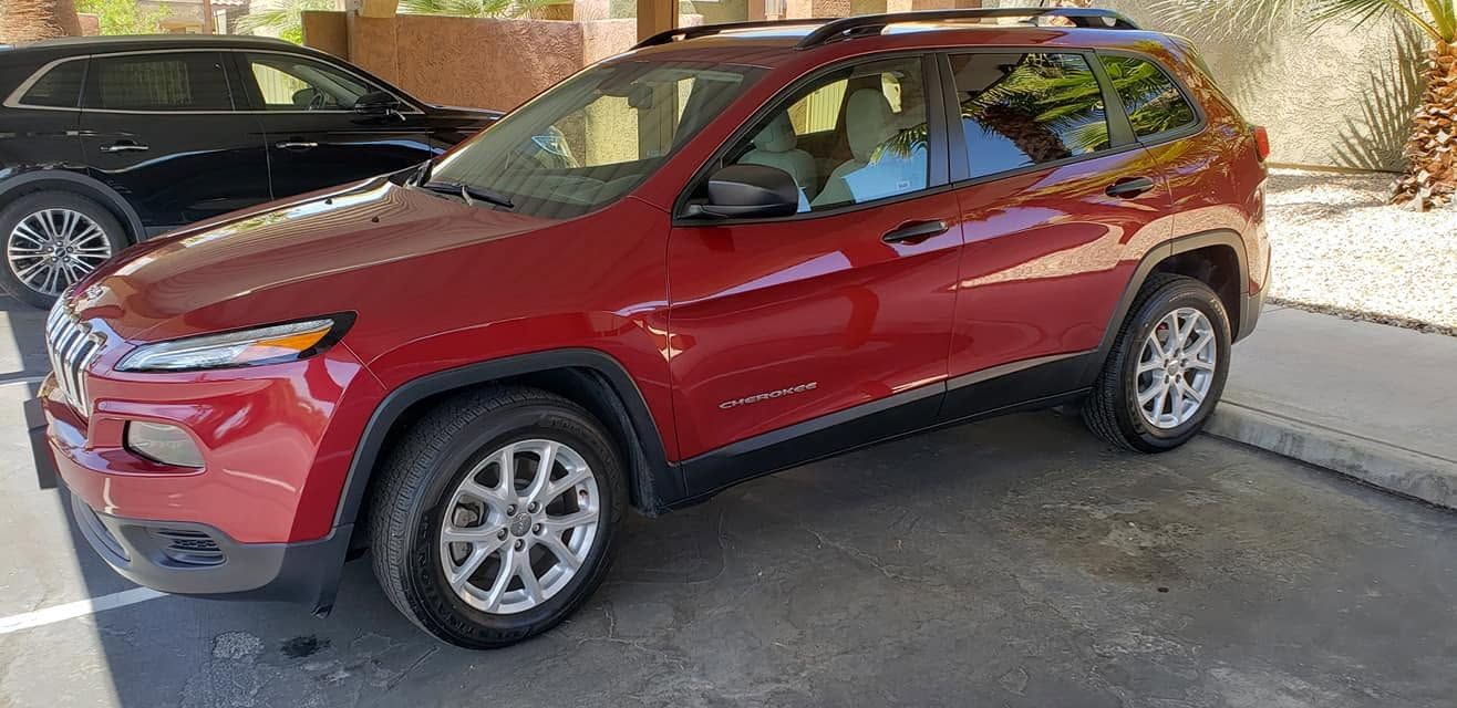 Red SUV parked in a lot beside another car, viewed from the front side.