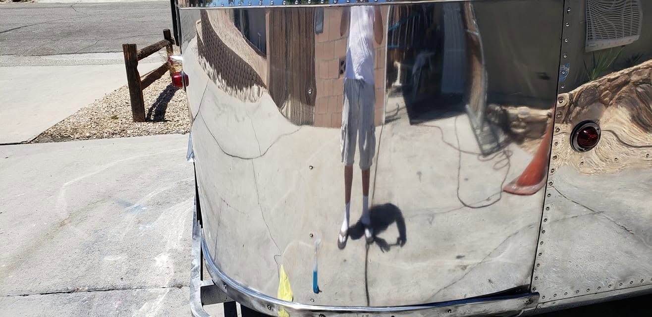 Shiny chrome trailer reflecting a person and outdoor pavement in bright sunlight