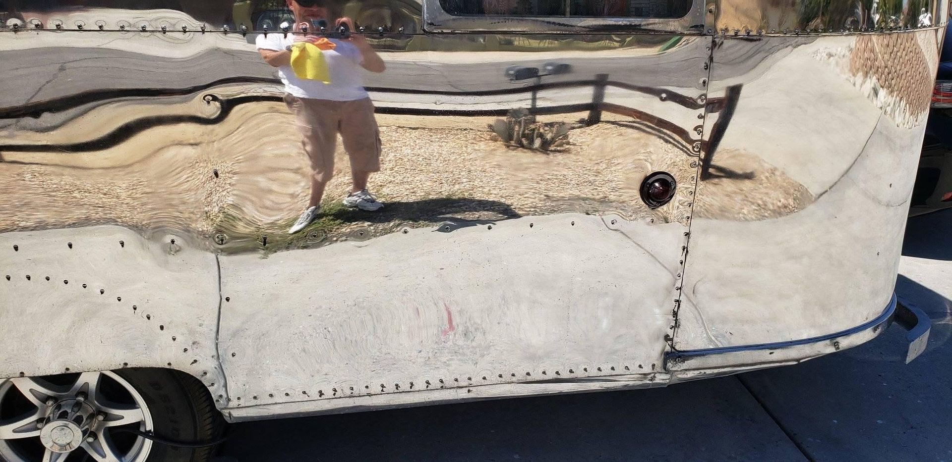 Dented white car door with shattered paint reflecting a person in a yellow shirt, beside a dark pavement.