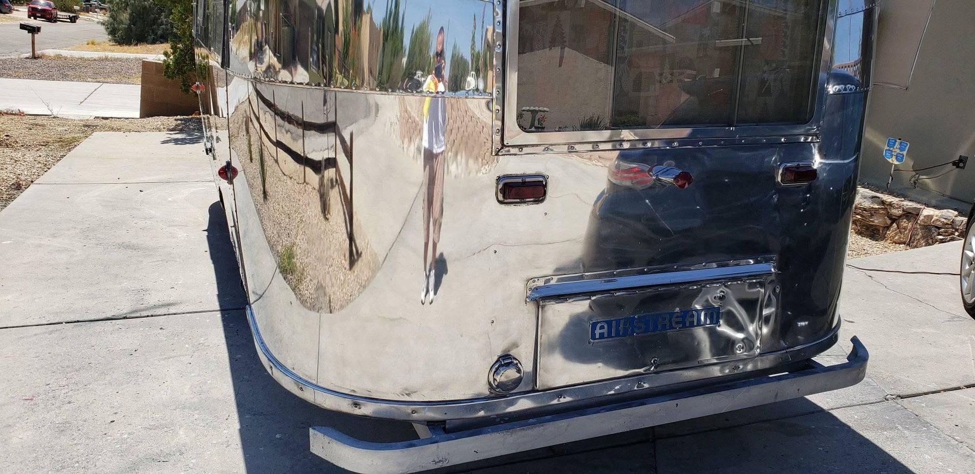 Shiny chrome rear of a bus reflecting a street and buildings in bright sunlight