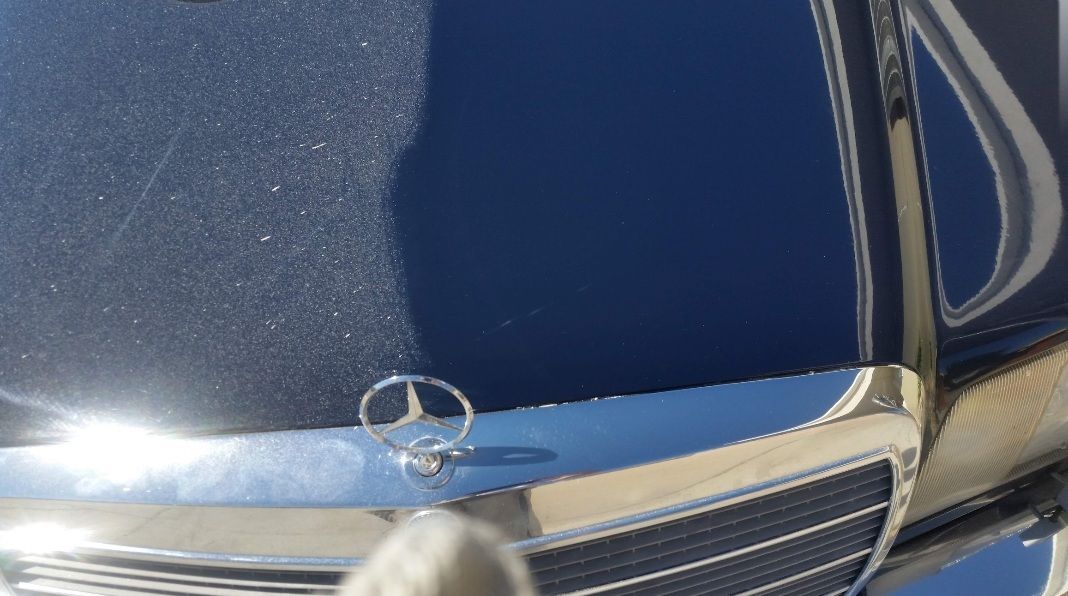 Front of a blue Mercedes-Benz with chrome grille and hood emblem, close-up view