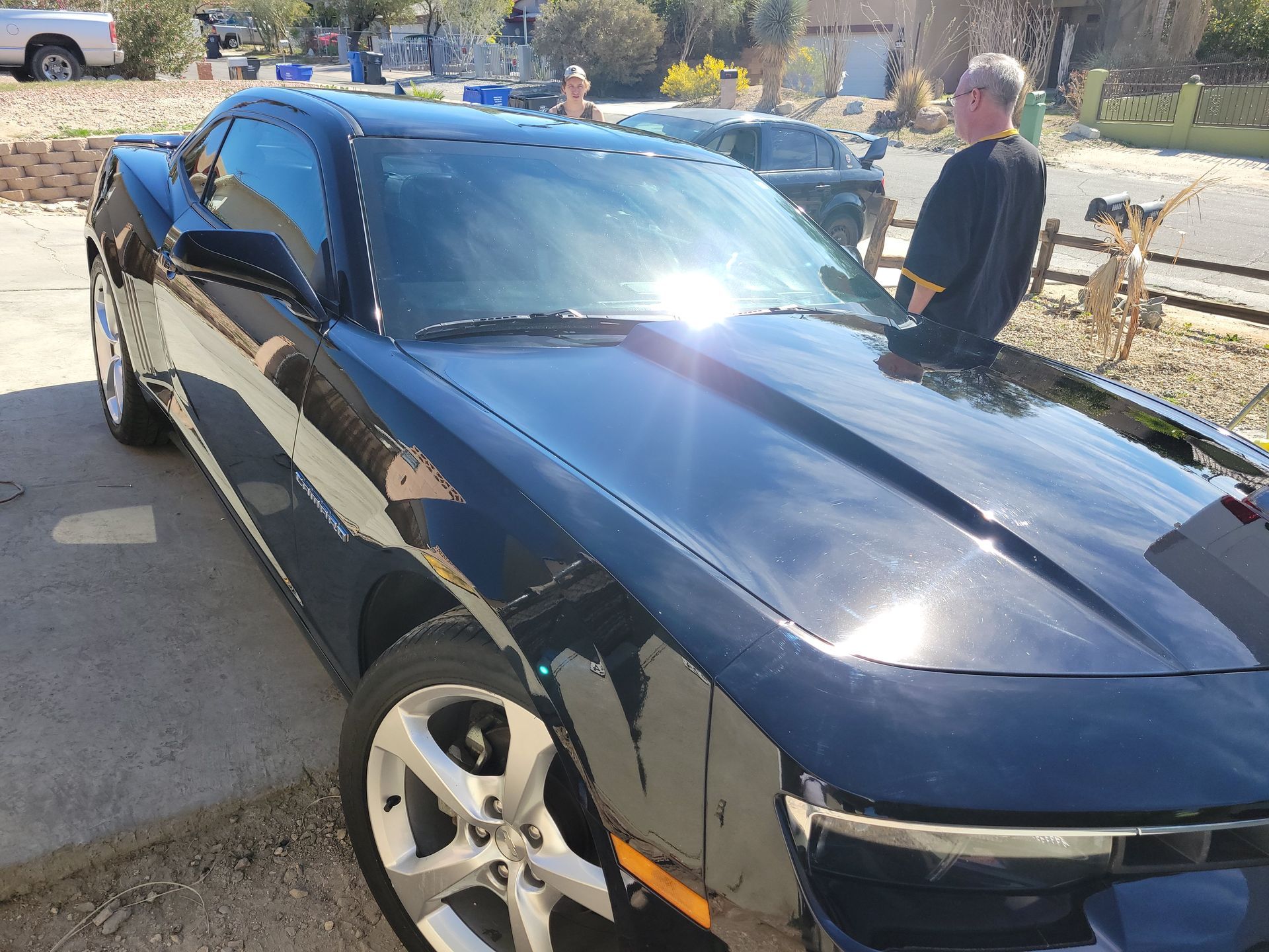 Black sports car parked in a driveway with a man standing beside it on a sunny day