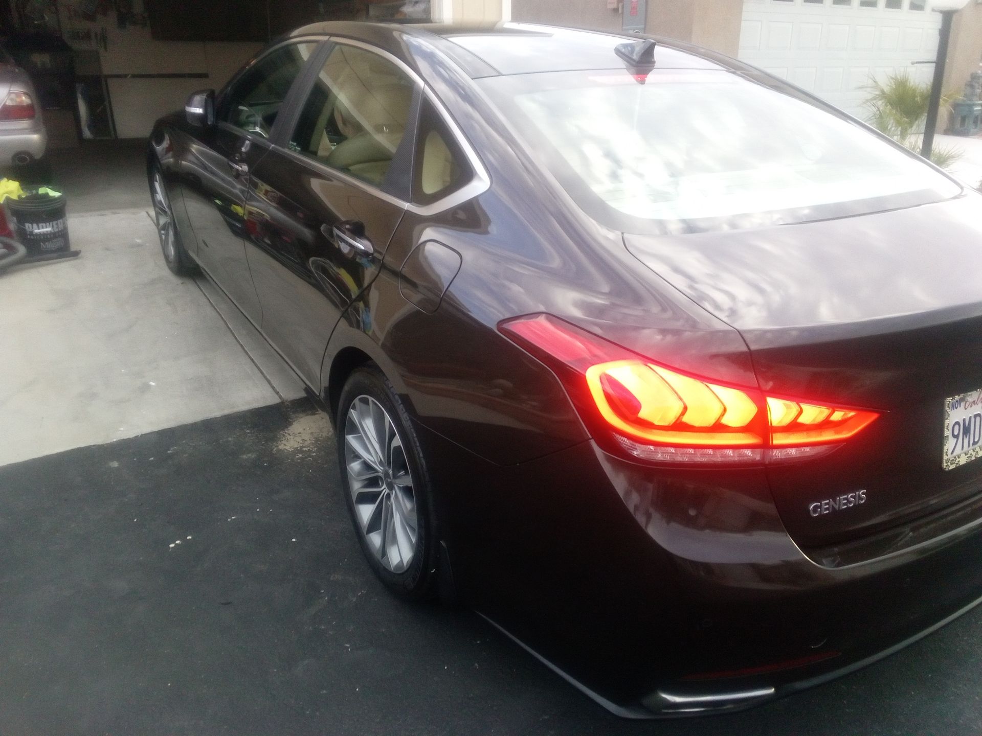 Dark sedan parked in a driveway, rear taillights glowing red.