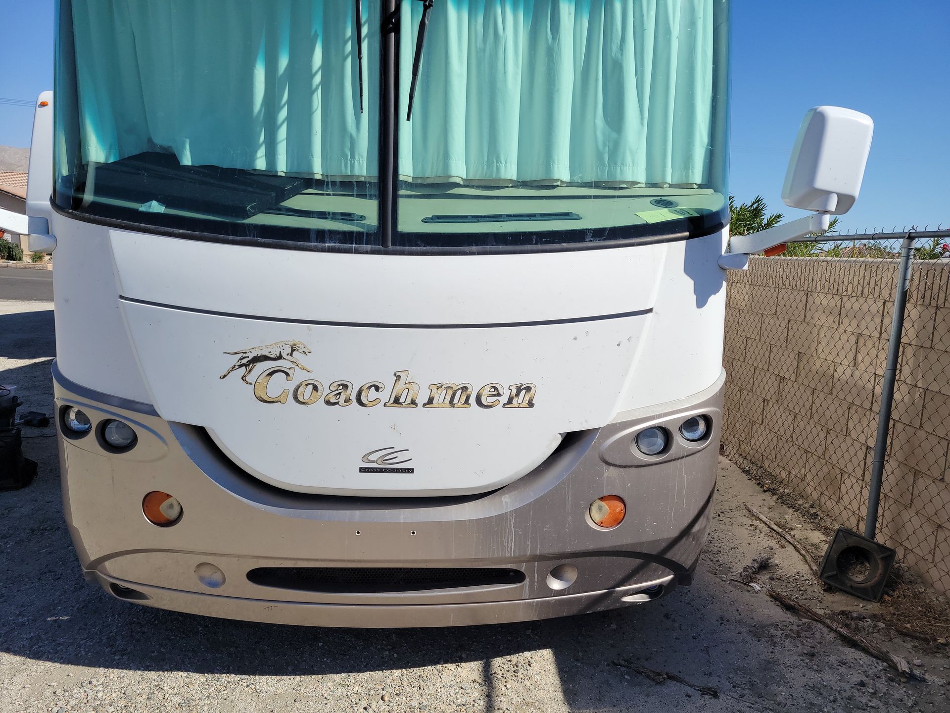 Front view of a white Coachmen vehicle parked beside a fence
