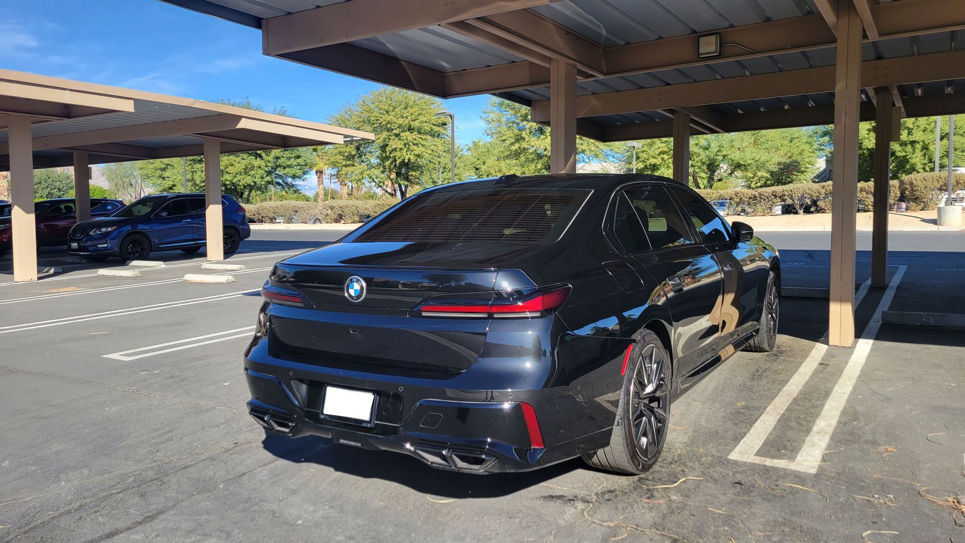 Black BMW sedan parked under a carport in a sunny lot.