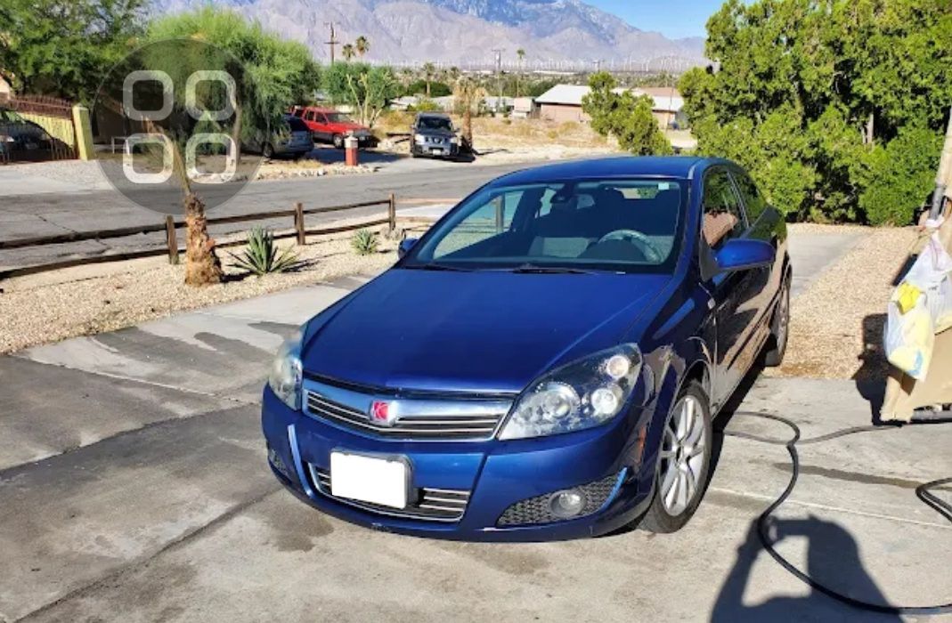 Blue sedan parked in a driveway beside a stone wall, with mountains in the background.