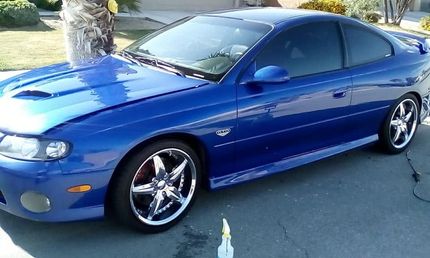 Blue sports coupe parked in a driveway, side view with chrome rims and tinted windows.