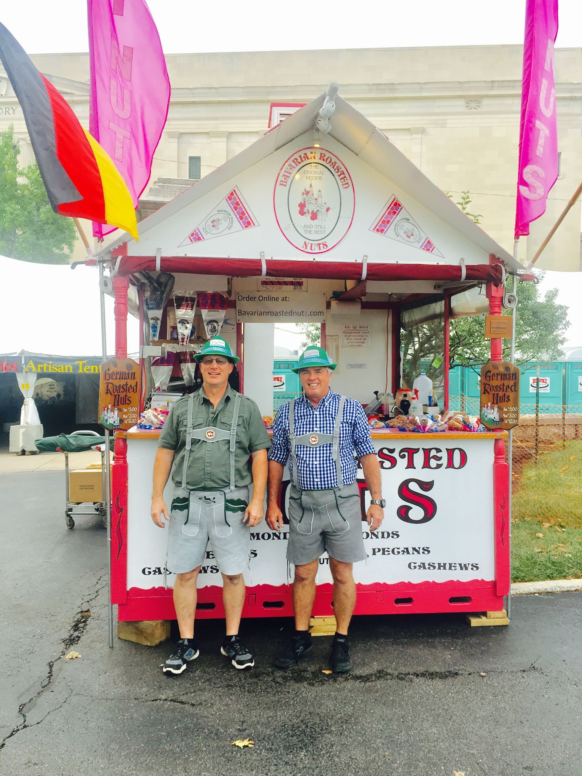 Two people standing in front of a pink and white festival booth on a wet street