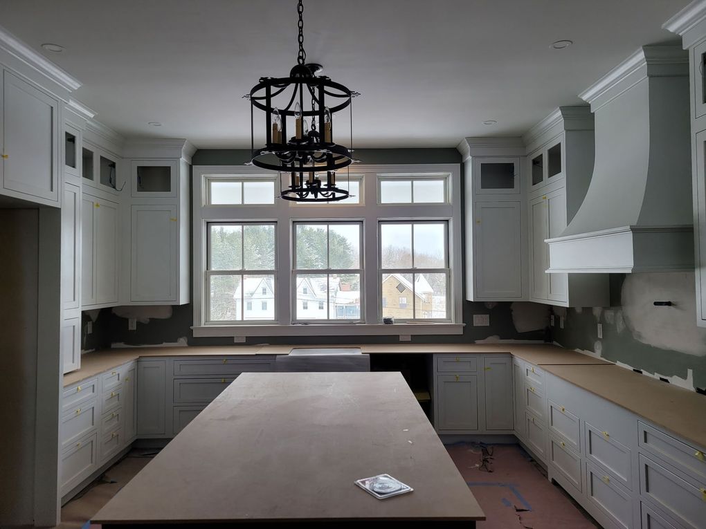 Bright empty kitchen with white cabinets, large island, and a window above the sink