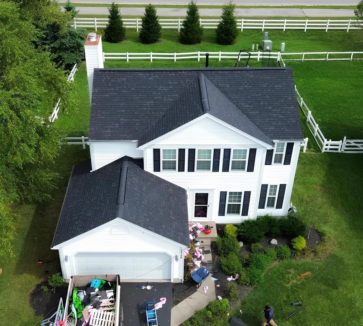 Aerial view of a white house with black roof, garage, and fenced green yard.