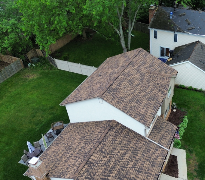 Aerial view of two tan-roofed houses beside a green backyard and white fence.