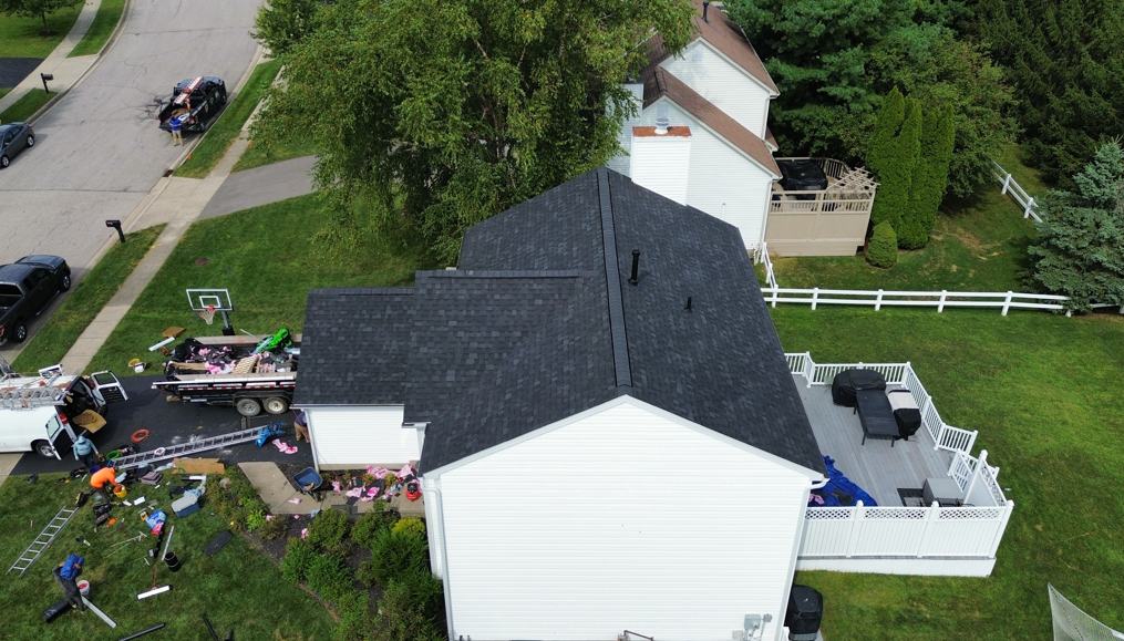 Aerial view of a white house with a black roof, debris and a damaged vehicle in the yard