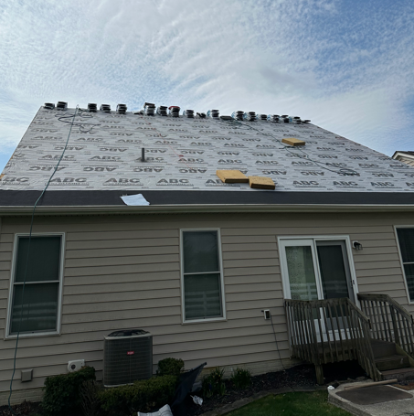 House roof under replacement with white underlayment and visible roofing materials on a cloudy day