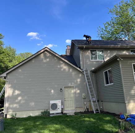 Worker on a roof repairing a gray house with a ladder against the wall on a sunny day