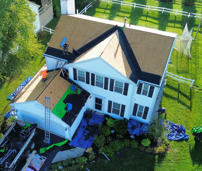 Aerial view of a white two-story house with a damaged lower section and debris in the yard.