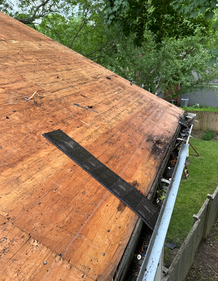 Roof edge with orange underlayment and black tape beside gutters and trees after damage