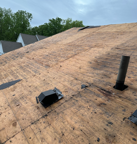 Partially covered roof with underlayment, vents, and a chimney pipe under a blue sky