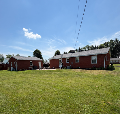 Red houses and outbuildings on a grassy lawn under a blue sky with power lines overhead