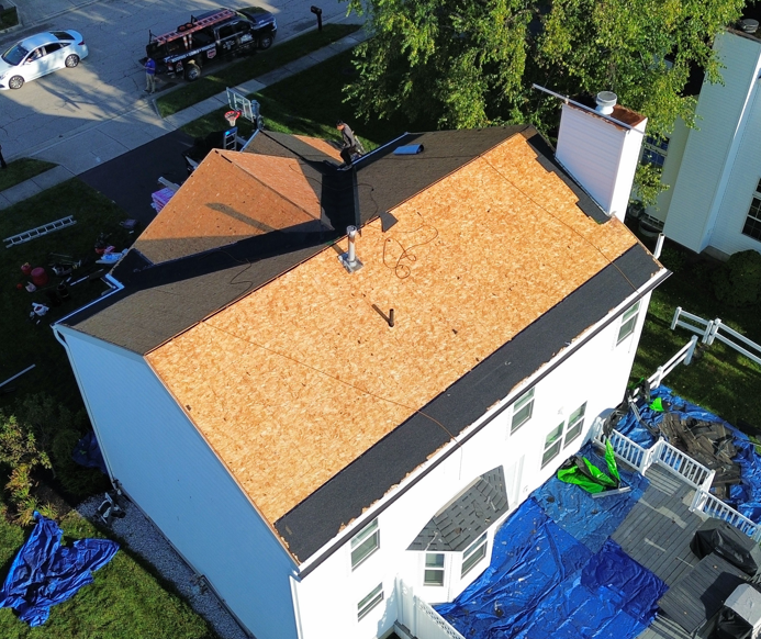 Aerial view of a house with a new tan roof being installed, with work materials around it.