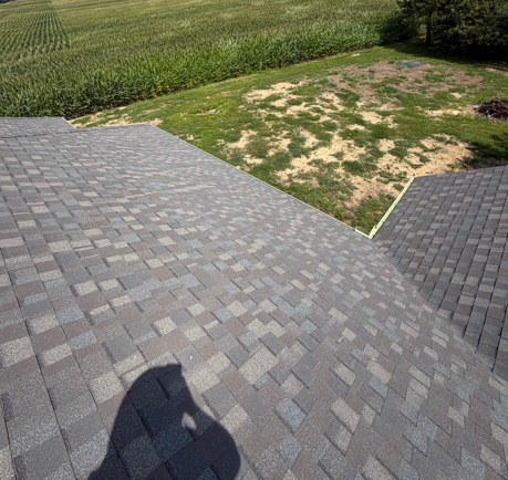 Gray shingled roof with a shadow, beside patchy grass and a cornfield on a sunny day