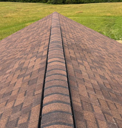 Brown shingled roof with a central ridge line, viewed from above against a grassy lawn.