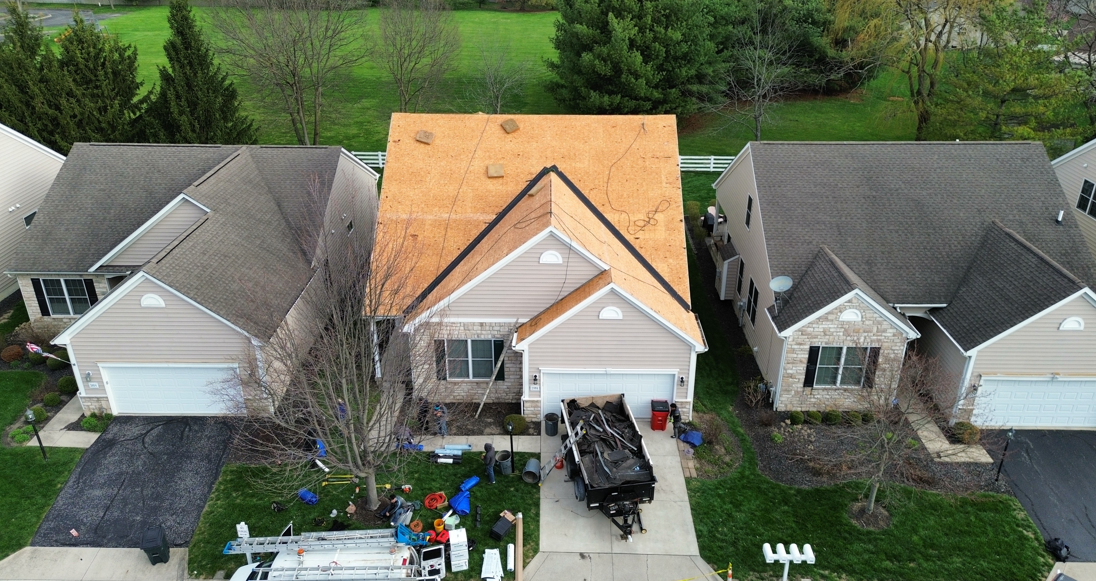 Aerial view of three suburban houses, with the center home’s roof under construction.