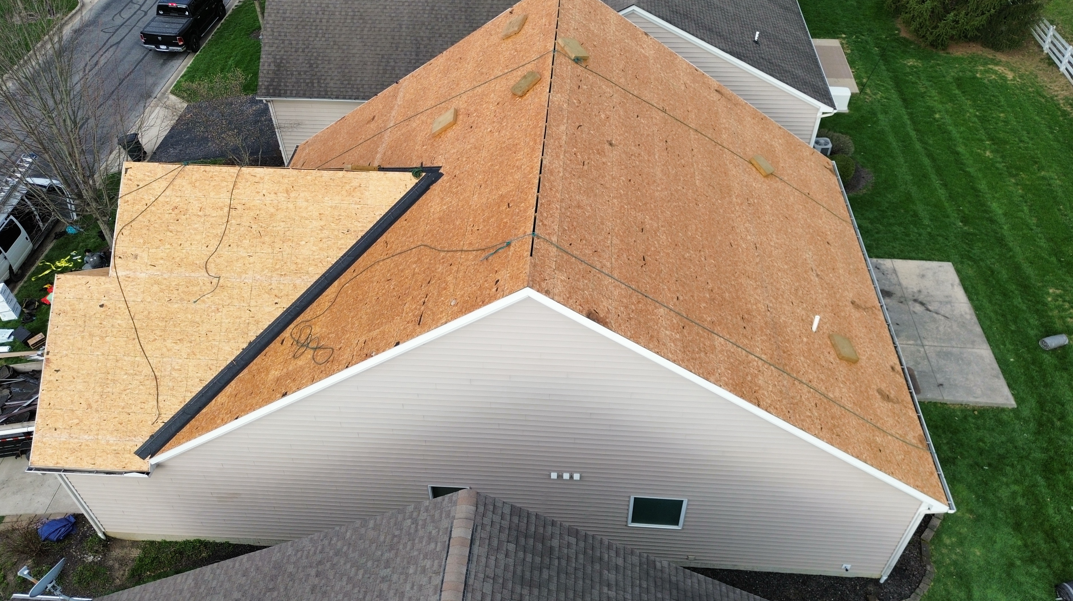 Aerial view of a house roof with tan shingles and a small section of darker roofing near a green lawn.