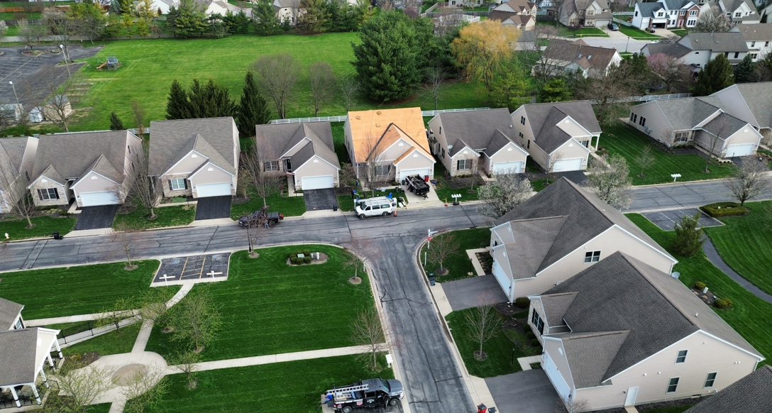 Aerial view of suburban houses along a curved street with green lawns and one tan-roofed home.