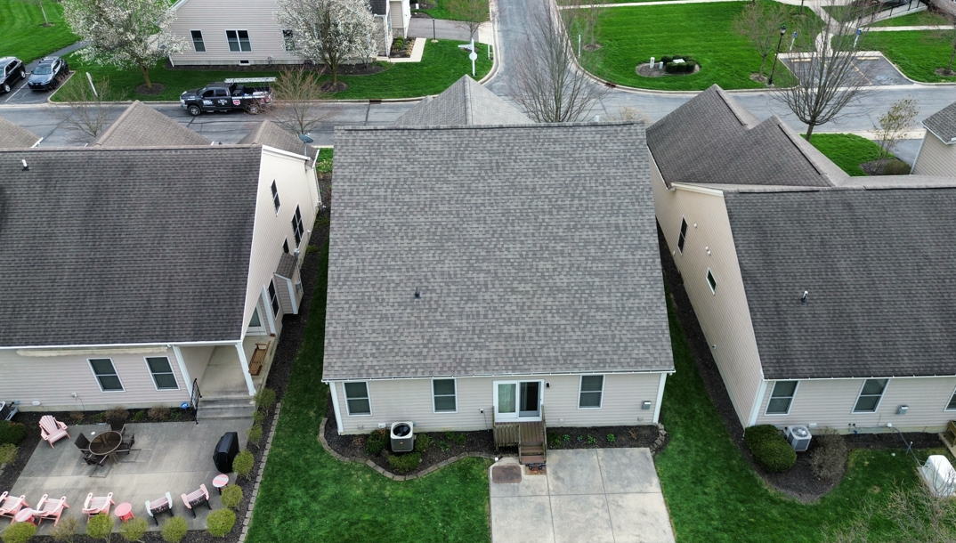 Aerial view of three beige houses with gray roofs and front lawns in a suburban neighborhood