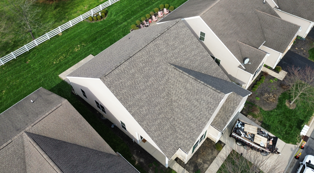 Aerial view of a gray-roofed suburban house with a driveway, lawn, and neighboring homes.
