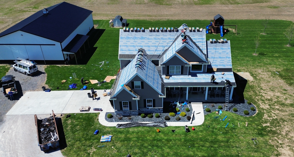 Aerial view of a gray farmhouse and large barn on a grassy rural property