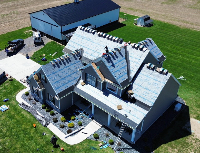 Aerial view of a large house with a gray roof and blue outbuilding on a green lawn