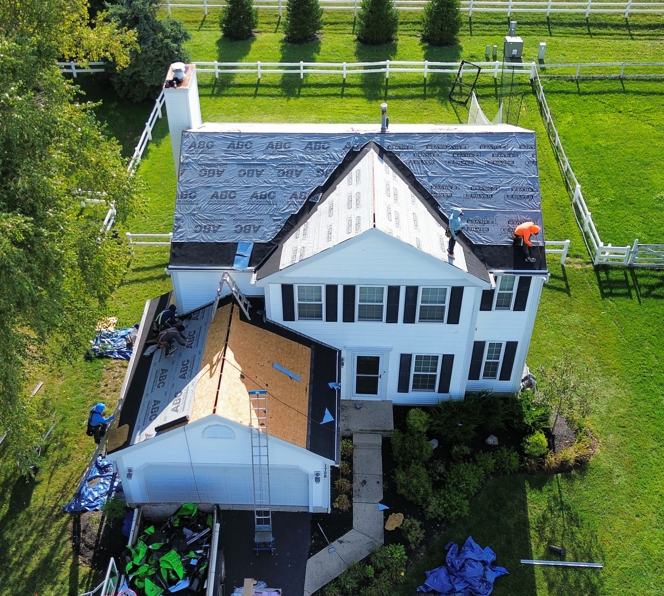 Aerial view of a white house with a dark roof, surrounded by green lawn and trees, with an attached garage.