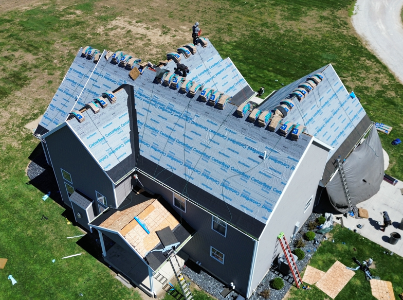 Aerial view of a house with a partially installed blue roof and exposed roof framing