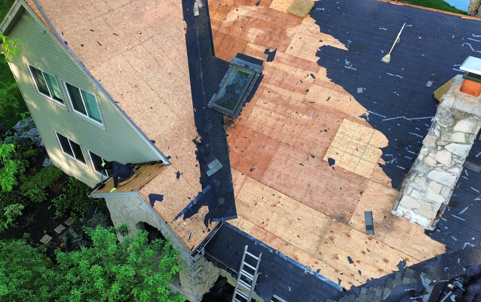 Aerial view of a roof under repair with plywood patches, a skylight, and a ladder near the edge