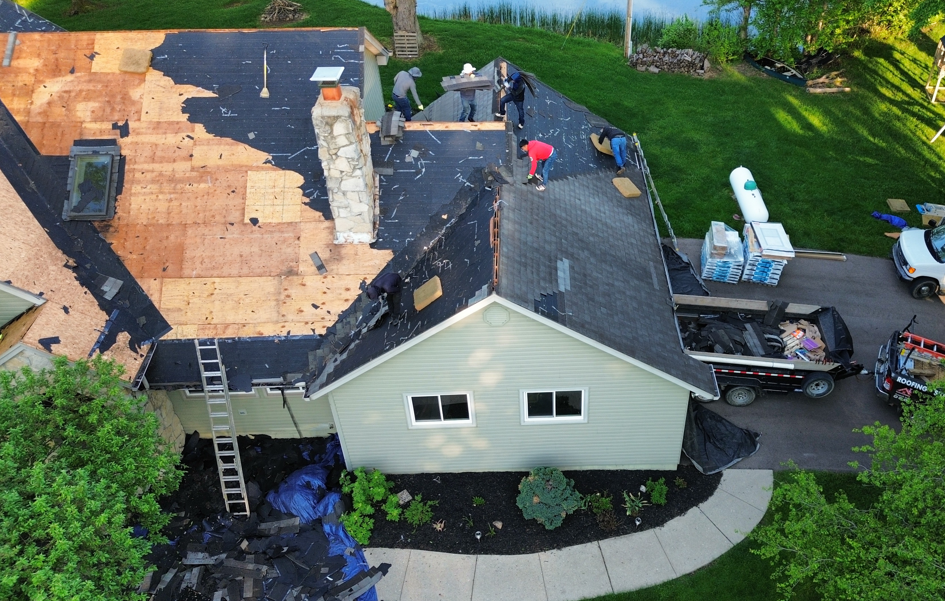 Aerial view of roofers repairing a home’s roof, with tools, ladders, and roofing materials visible.