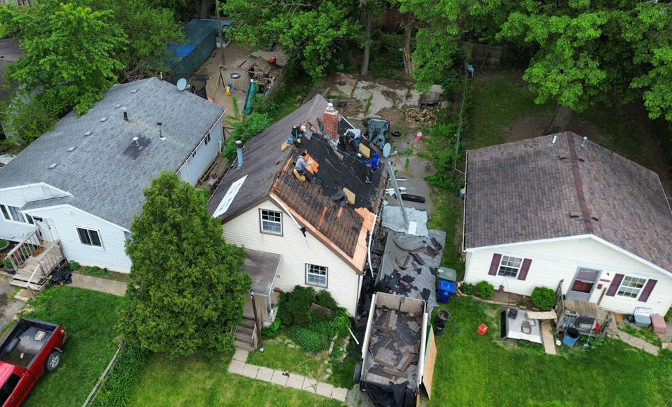 Aerial view of homes with roof damage and workers repairing one roof after a storm