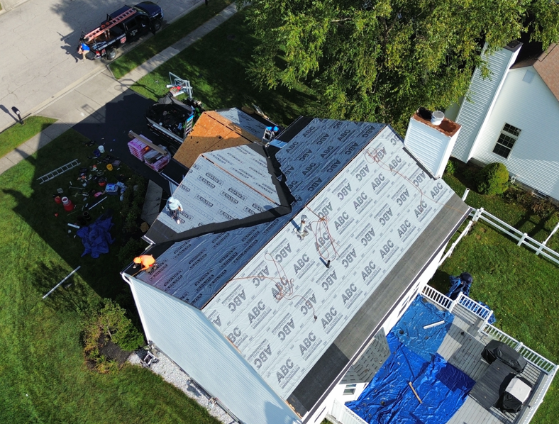 Aerial view of a house roof being re-shingled, with workers and materials around it