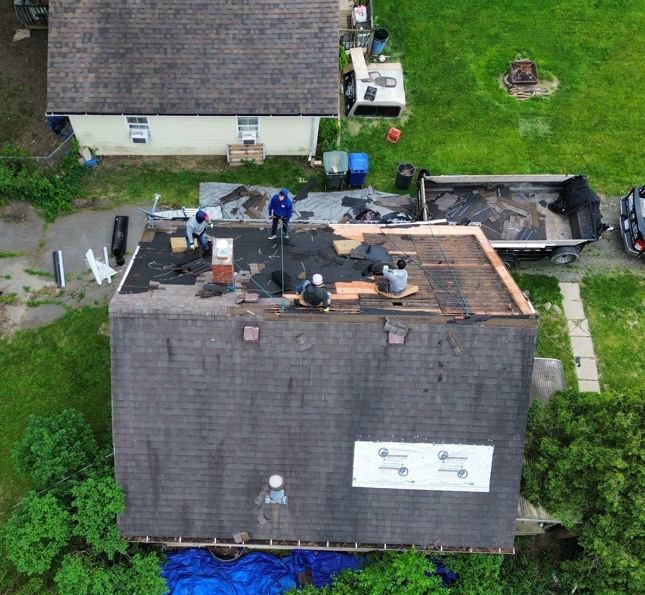Aerial view of roofers repairing a shingled house roof with tools and debris on top.