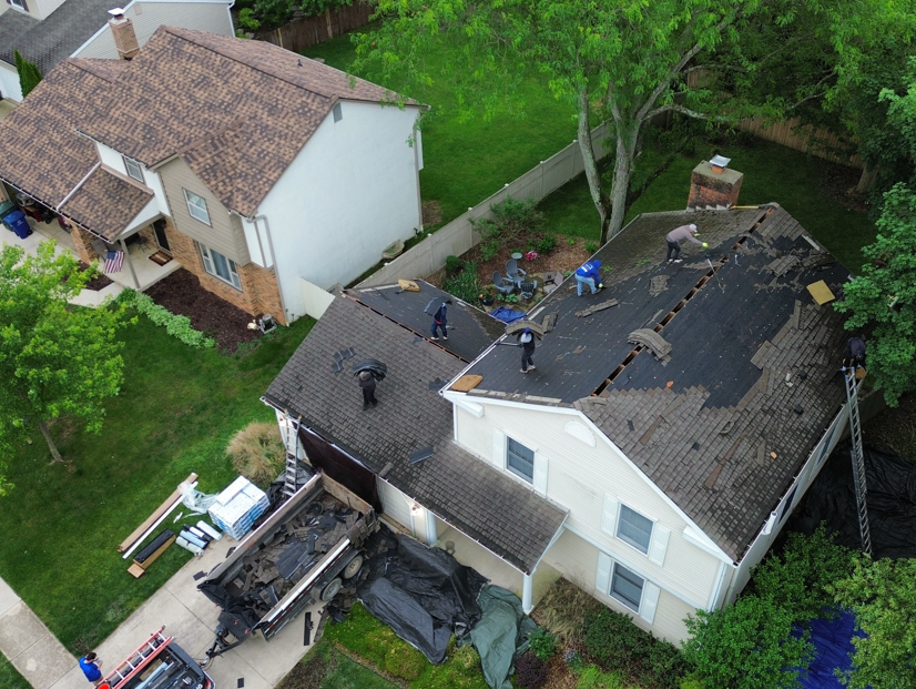 Aerial view of a damaged house roof with missing shingles and visible debris after a storm.
