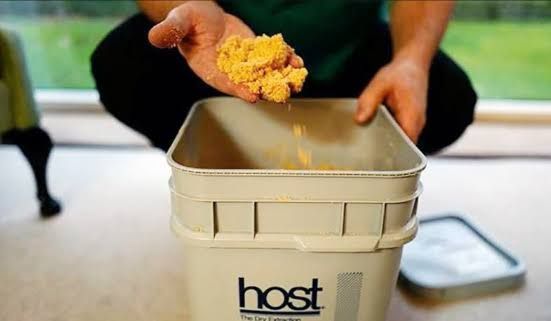 Hands dropping yellow sponge into a beige bucket labeled “host” on a kitchen floor